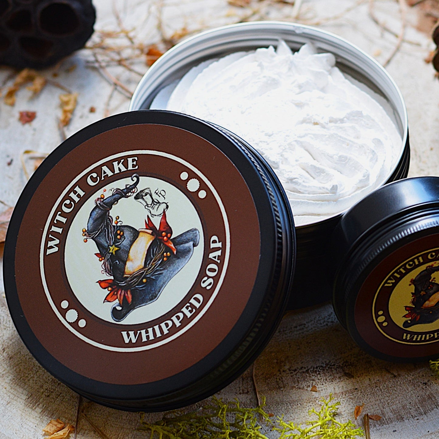 Witch Cake whipped soap in a container on a natural wooden surface with decorative elements.