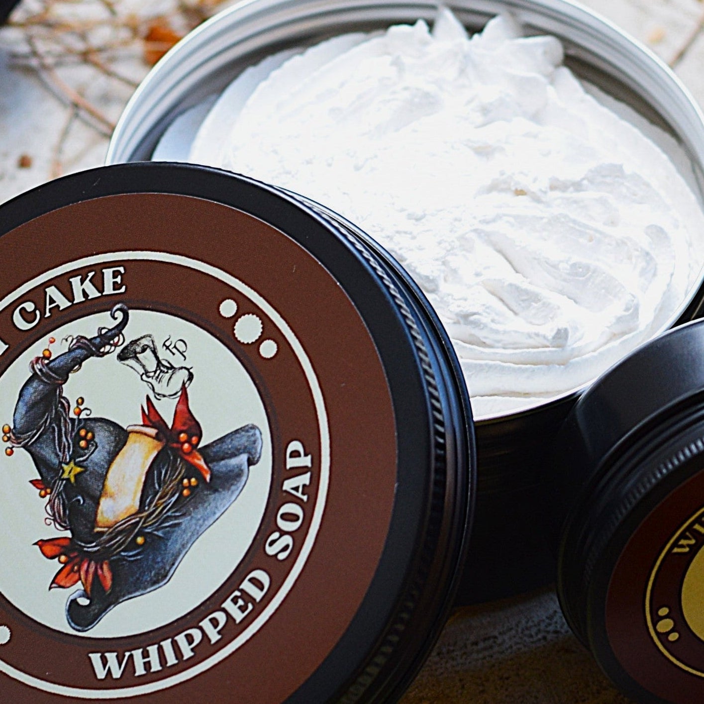 Witch Cake whipped soap in a container on a natural wooden surface with decorative elements.
