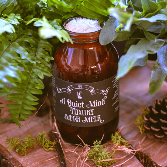 Bottle of 'A Quiet Mind' luxury bath milk with a label, surrounded by greenery on a wooden surface.