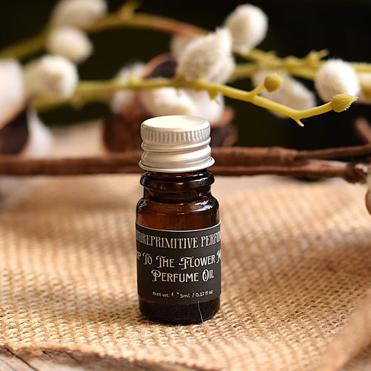 an amber glass bottle of A trip to the flower market perfume oil by futureprimitive soap sitting on burlap fabric with cotton flowers blurred in the background 