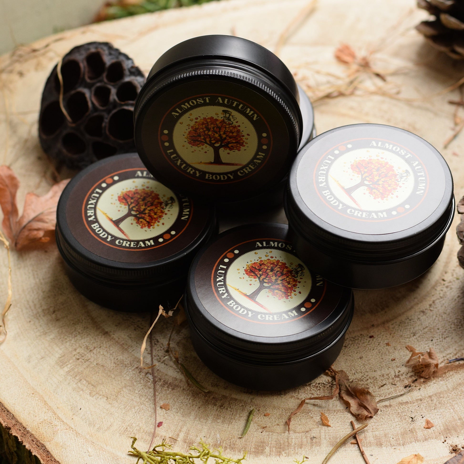 Black tins of Luxury Body Cream on a wooden surface with natural elements.