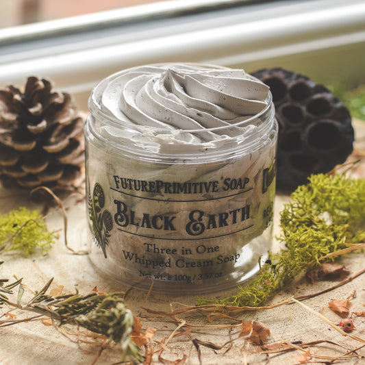 Black Earth Whipped soap sat on a wooden table surrounded by dried moss and pine cones