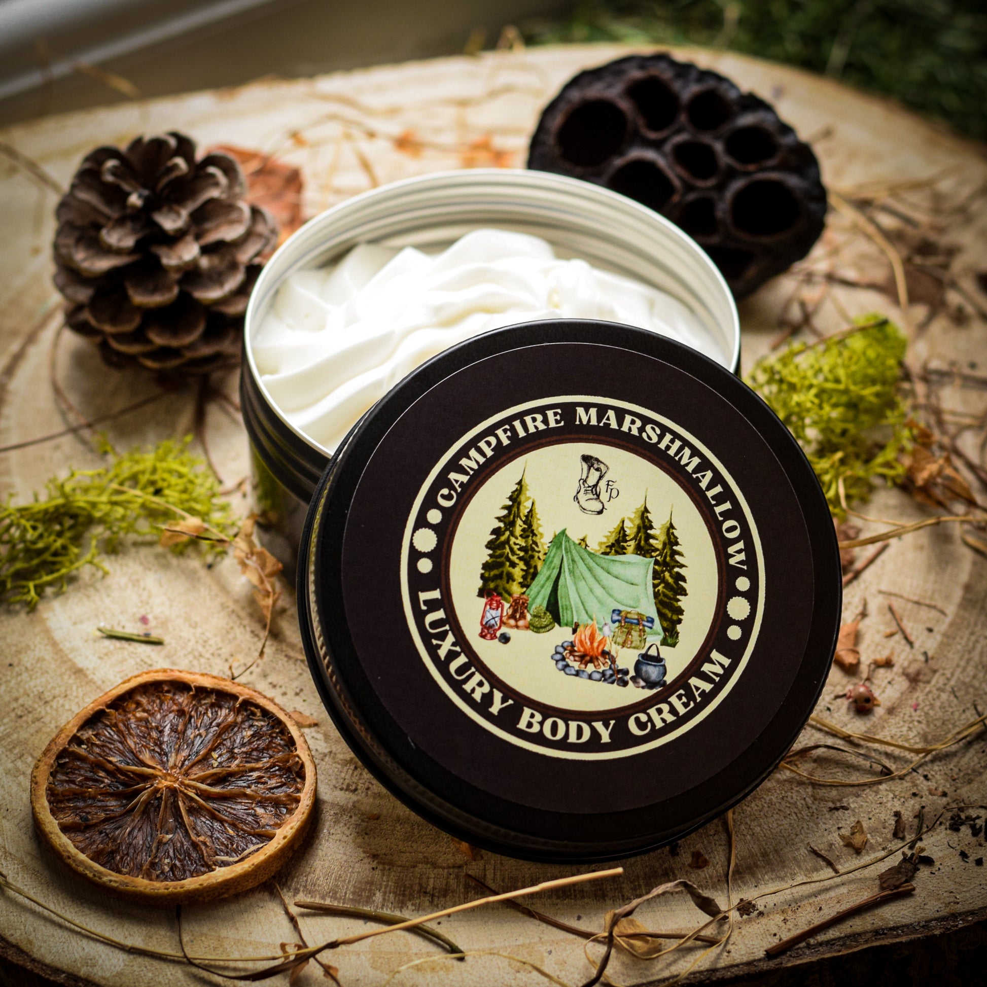 Open container of Campfire Marshmallow Luxury Body Cream on a rustic surface with natural elements.