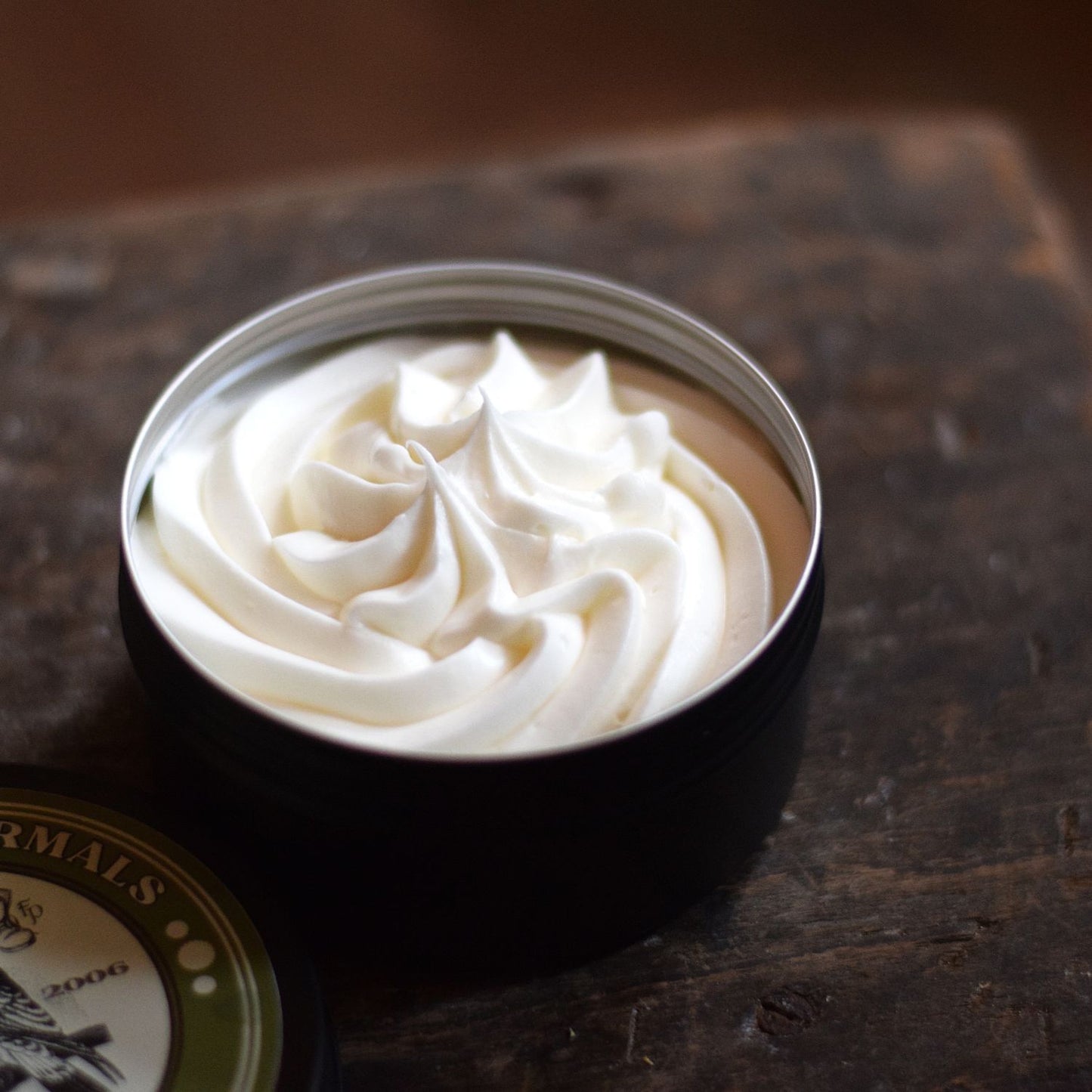 piped body butter in a tin sat on a wooden surface