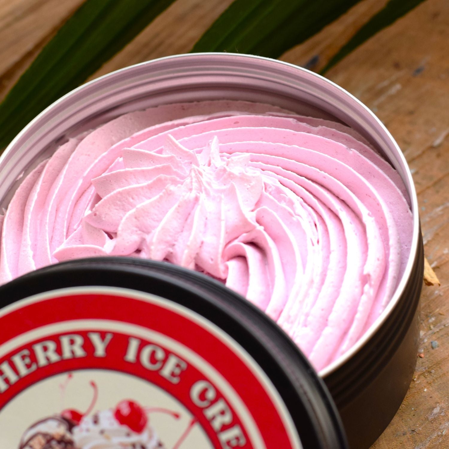 Pink whipped soap in a container with a cherry ice cream label on a wooden surface