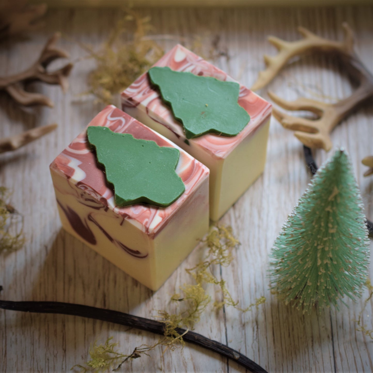 Two soap bars with green tree-shaped cutouts on a wooden surface with decorative elements.