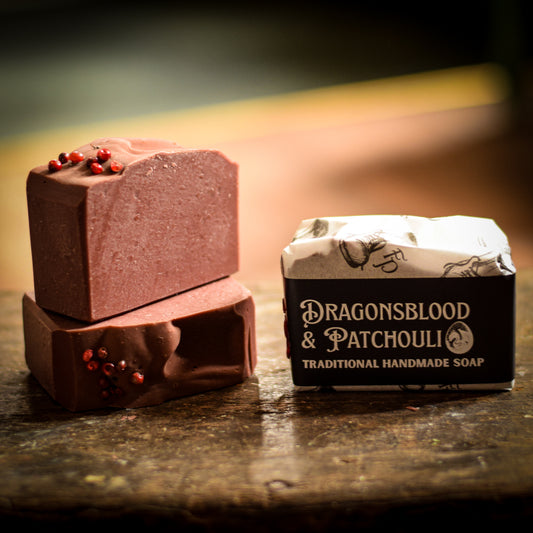Two pieces of red clay soap with a box labeled 'Dragonsblood & Patchouli' on a wooden surface.