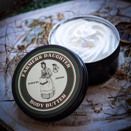 Open container of Farmers Daughter body butter on a rustic surface with dried plants.
