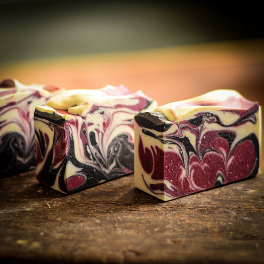 Three bars of purple marbled soap on a wooden surface with a blurred background