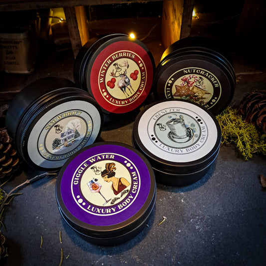 Collection of luxury body cream tins with decorative labels on a dark surface.