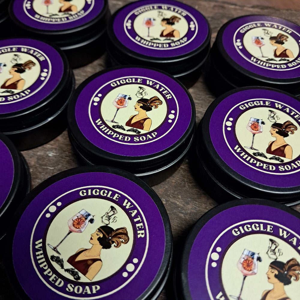 Mini tins of Giggle Water Whipped Soap on a wooden surface
