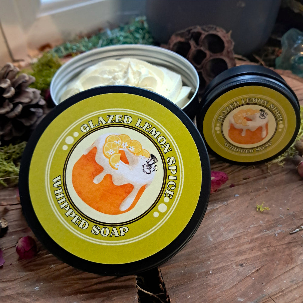 Two containers of 'Glazed Lemon Spice' whipped soap on a wooden surface with decorative elements.