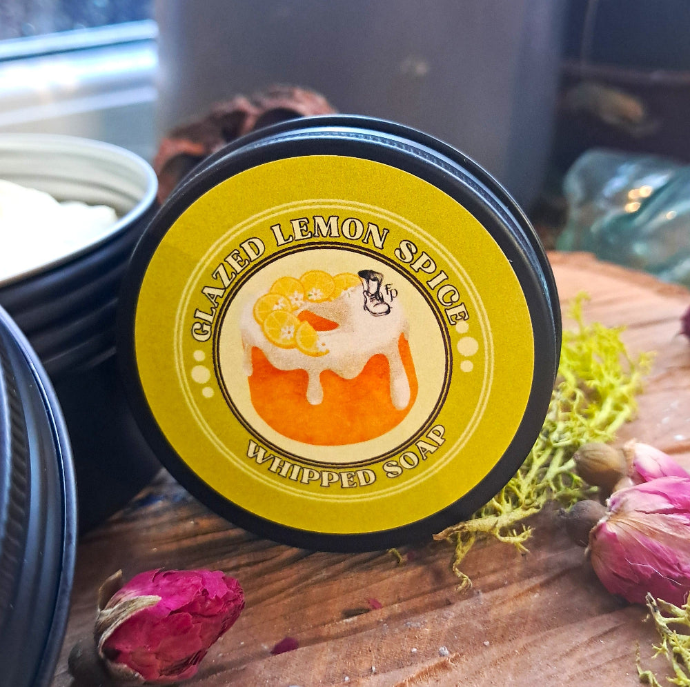 Container of glazed lemon spice whipped soap on a wooden surface with decorative elements.