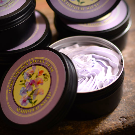Whipped soap in a black tin with a purple lid on a wooden surface