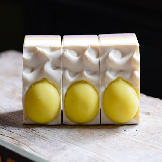 lemon handmade soap with lemon soaps on the top of each bar. the soap is sitting on a rustic wooden surface with a black background.