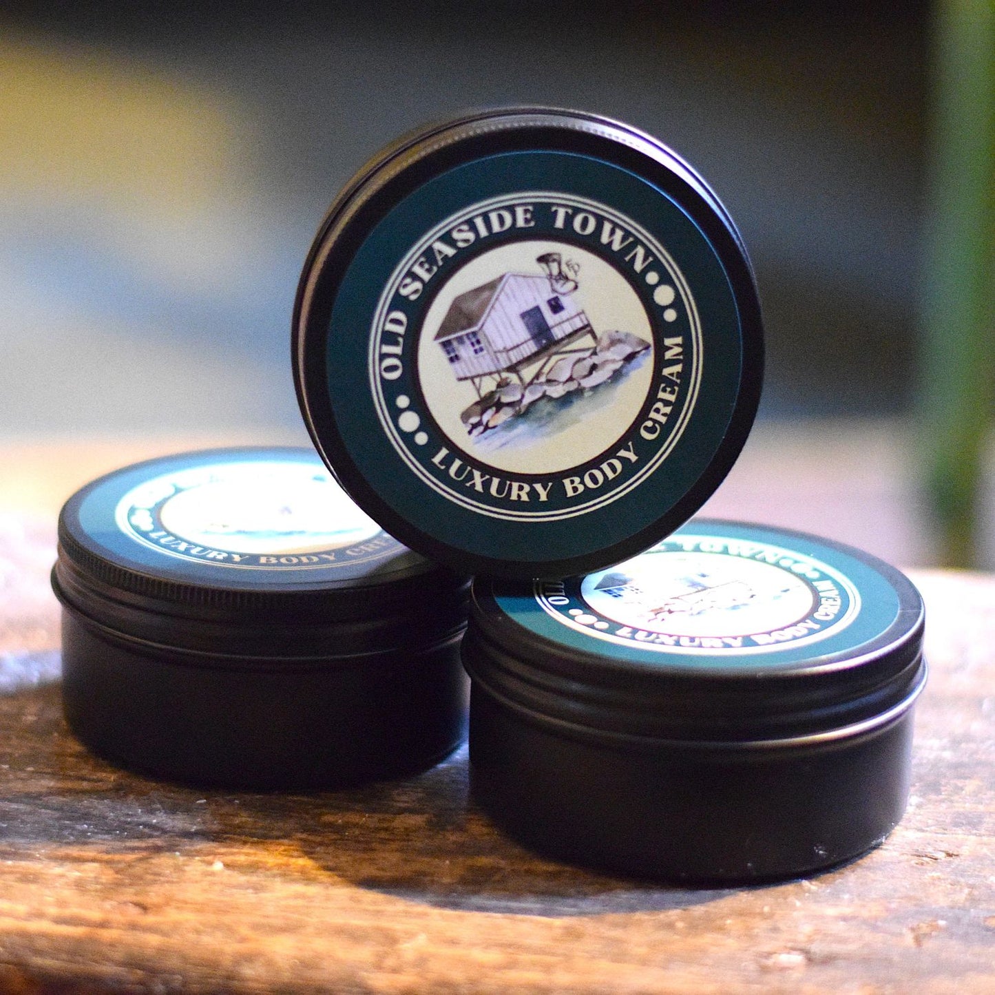 Three tins of Old Seaside Town Luxury Body Cream stacked on a wooden surface.