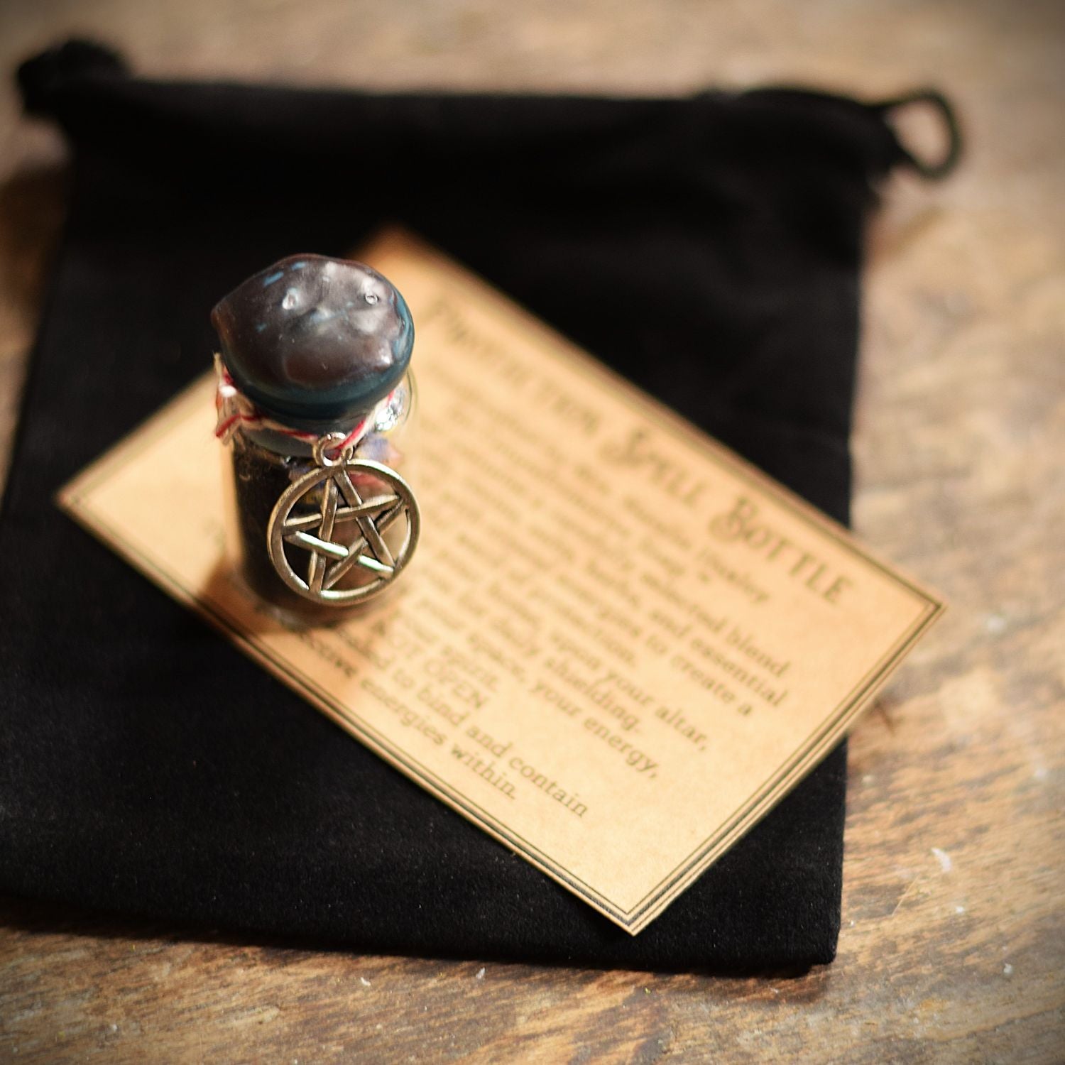 Small glass bottle with a pentacle charm on a black cloth with text