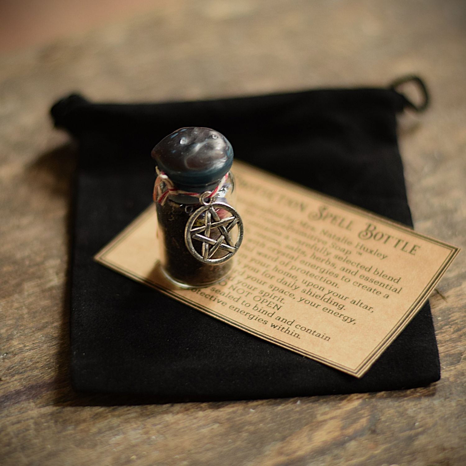 Small glass bottle with a pentagram design on a black cloth with text
