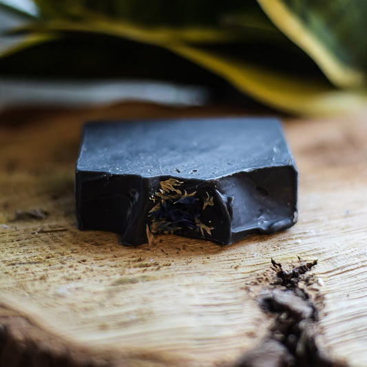 Dark soap bar with natural elements on a wooden surface