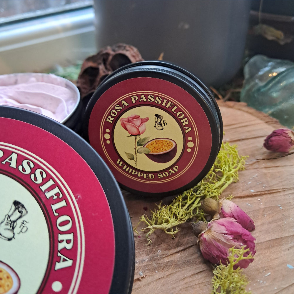 Two containers of Passiflora whipped soap on a wooden surface with dried flowers.