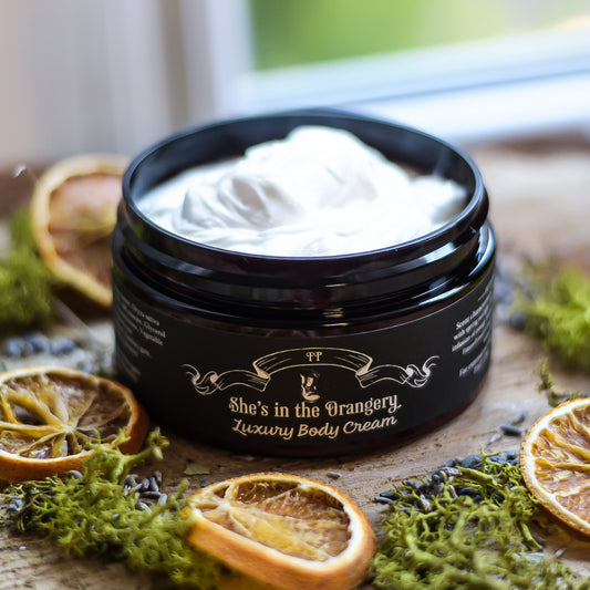 Jar of 'She's in the Orangery' luxury body cream on a wooden surface with dried oranges and lavender.