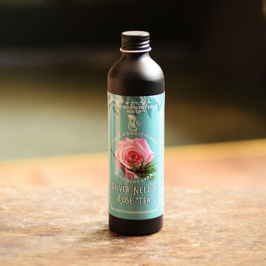 Bottle of Silver Needle Rose Tea hair conditioner on a wooden surface with a blurred background