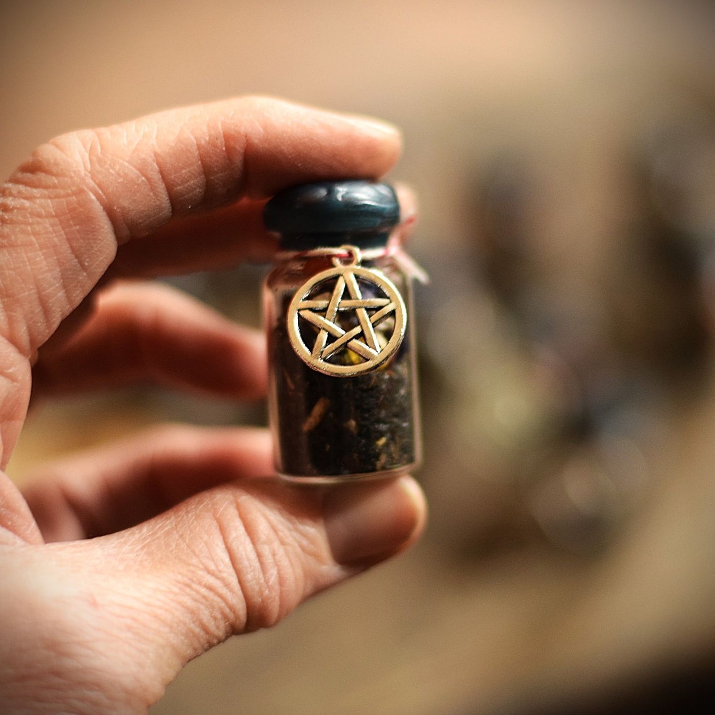 Hand holding a small glass jar with a pentagram charm against a blurred background