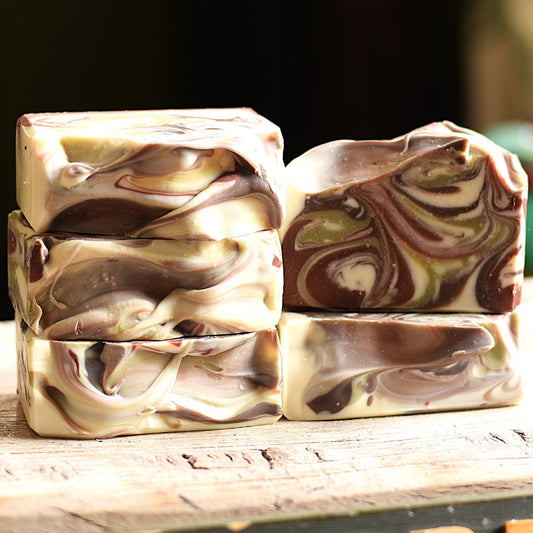 Four marbled artisan soap bars stacked on a rustic wooden surface with a dark, blurred background.