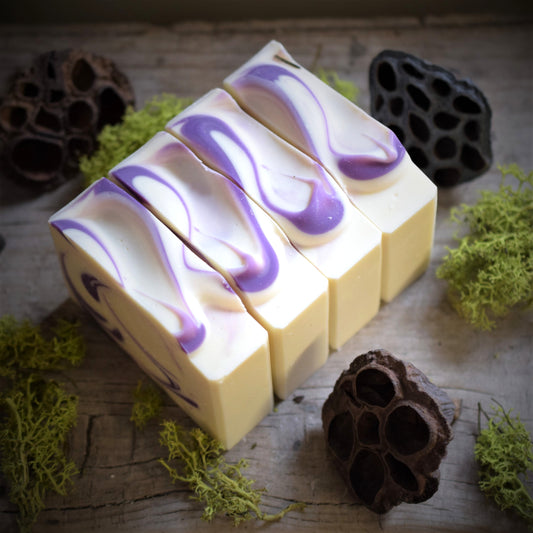 Three bars of soap with purple swirls on a wooden surface with natural elements.