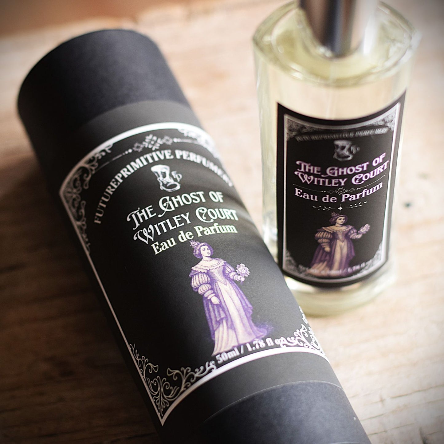 A perfume bottle and its cylindrical packaging tube for 'The Ghost of Whitley Court' Eau de Parfum by FuturePrimitive Perfum, displayed on a rustic wooden surface.