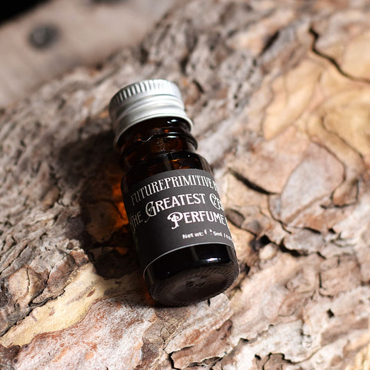 A small amber glass bottle of Future Primitive 'The Greatest Cedar of All Perfume' with a silver cap and black label, resting on textured tree bark.
