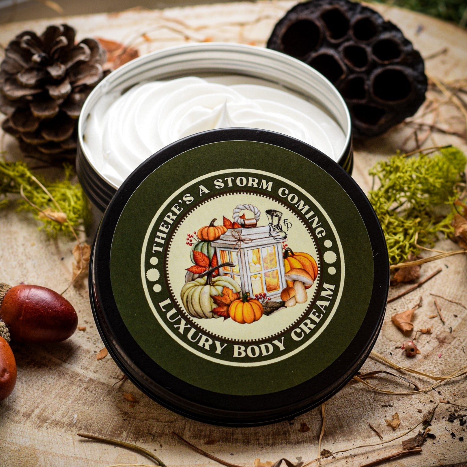 Open jar of luxury body cream with decorative lid featuring pumpkins and text, surrounded by natural elements.