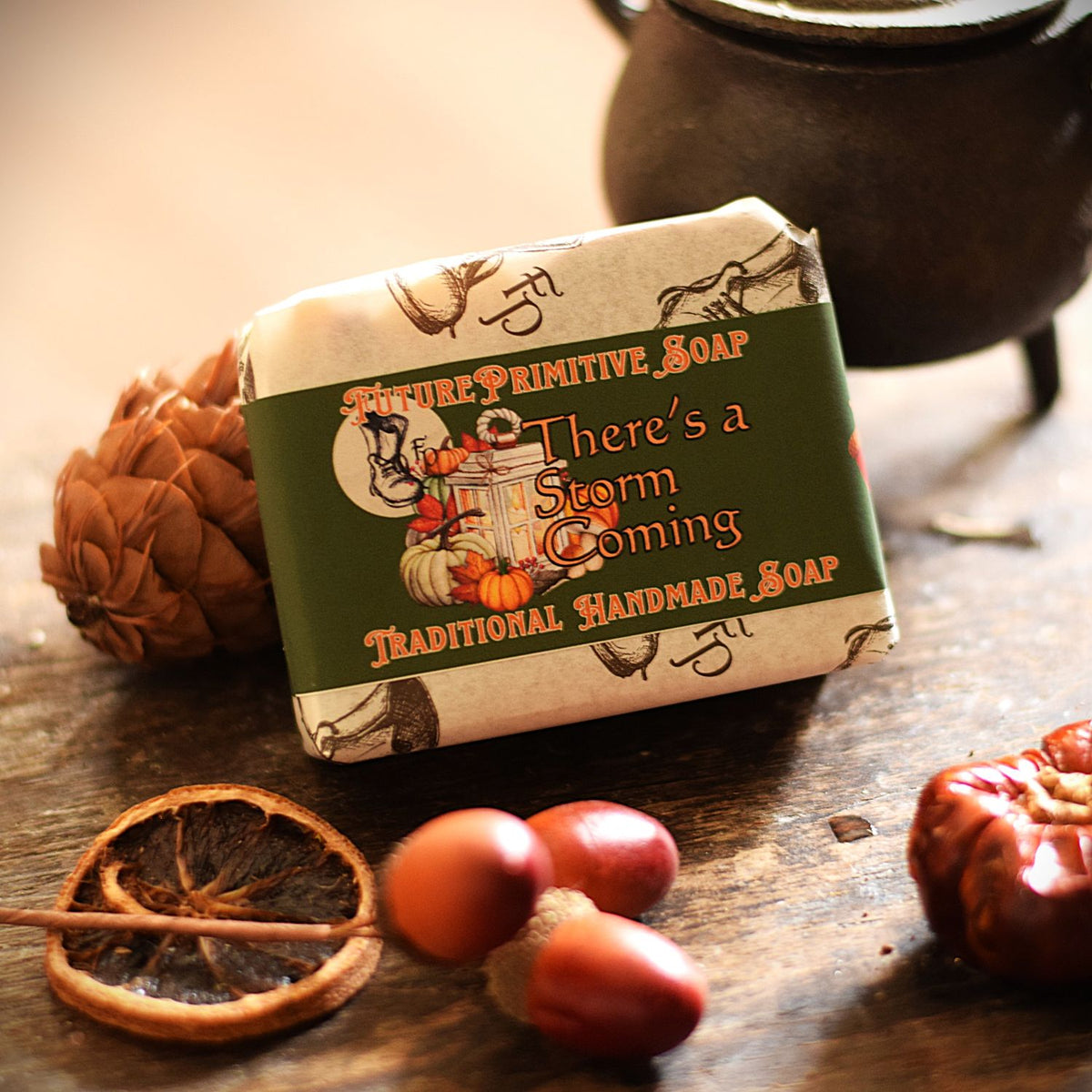 A wrapped bar of soap from FuturePrimitive Soap sits on a rustic wooden surface with autumn props including a dried orange slice, acorns, and a dark metal pot in the background.