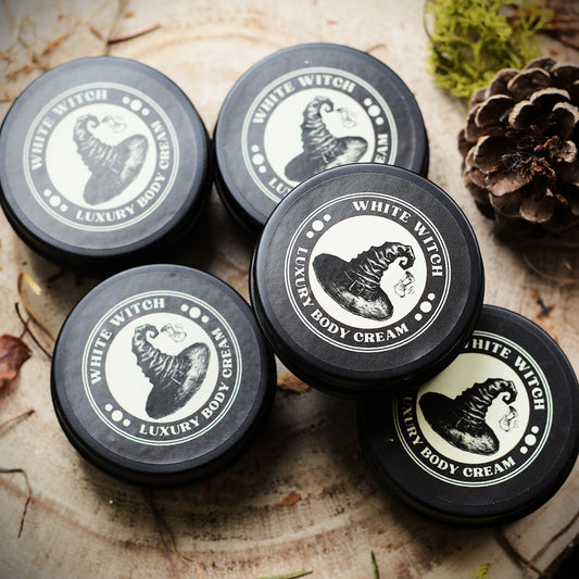 Five containers of White Witch Luxury Body Cream on a wooden surface with natural elements.