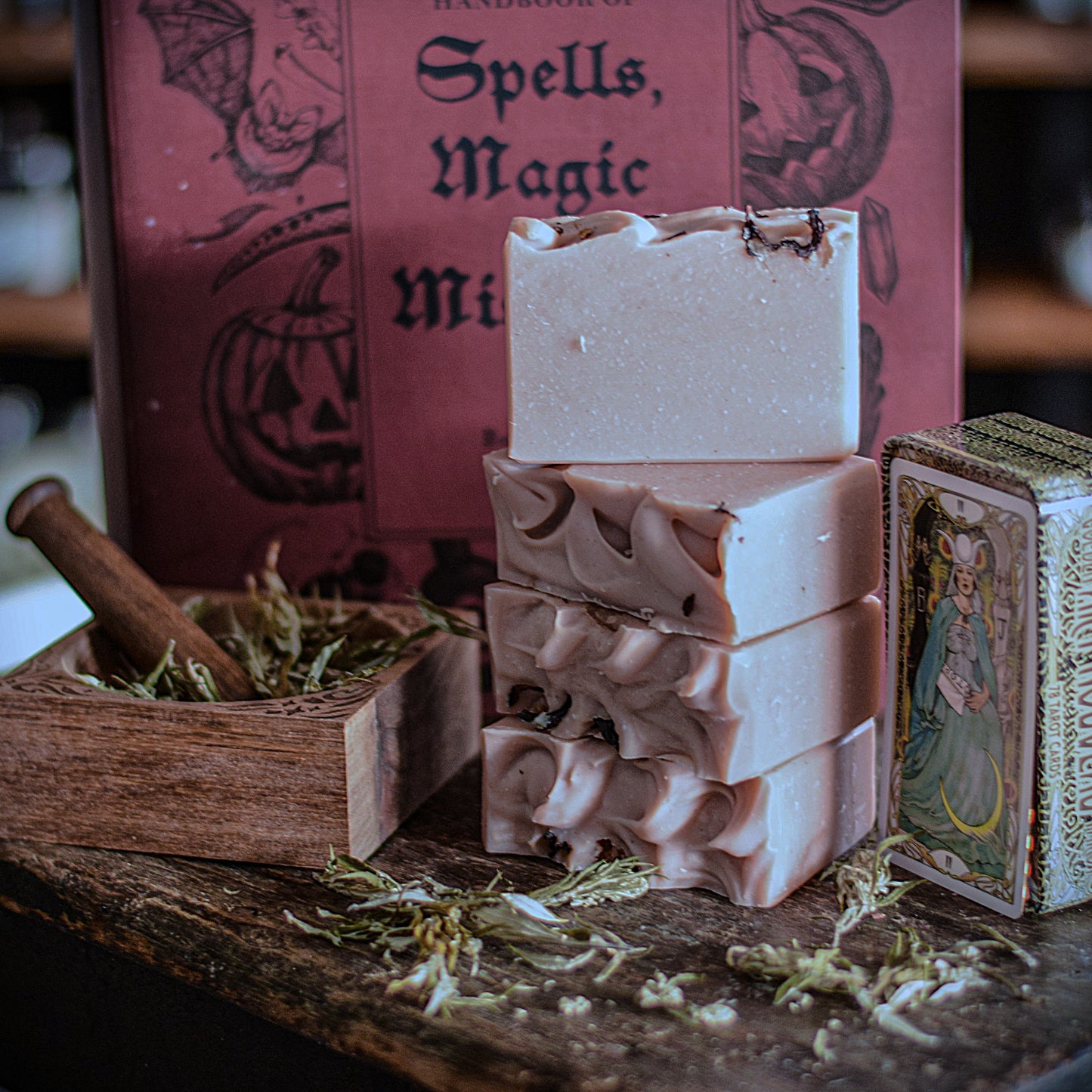 Three stacked soap bars on a wooden surface with a book and other items in the background.