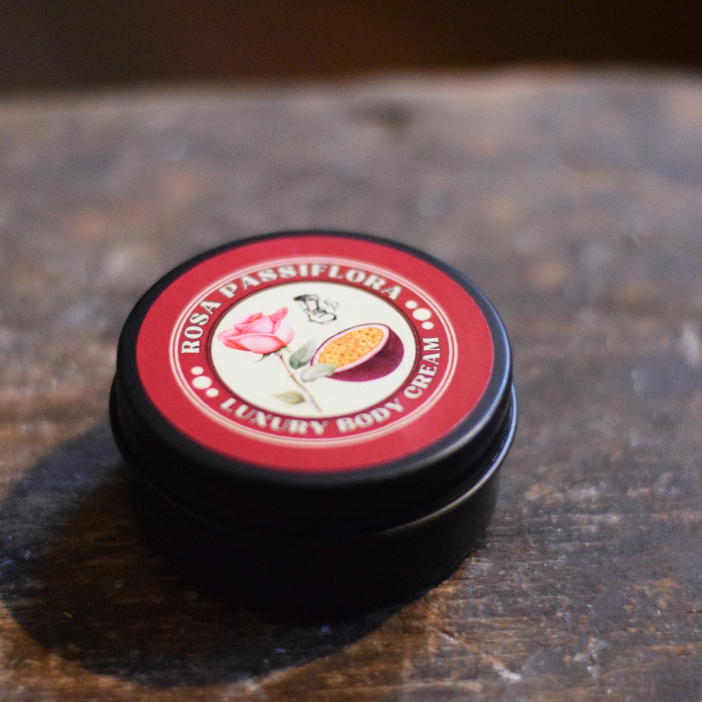 Two black tins with red lids featuring a floral design on a wooden surface