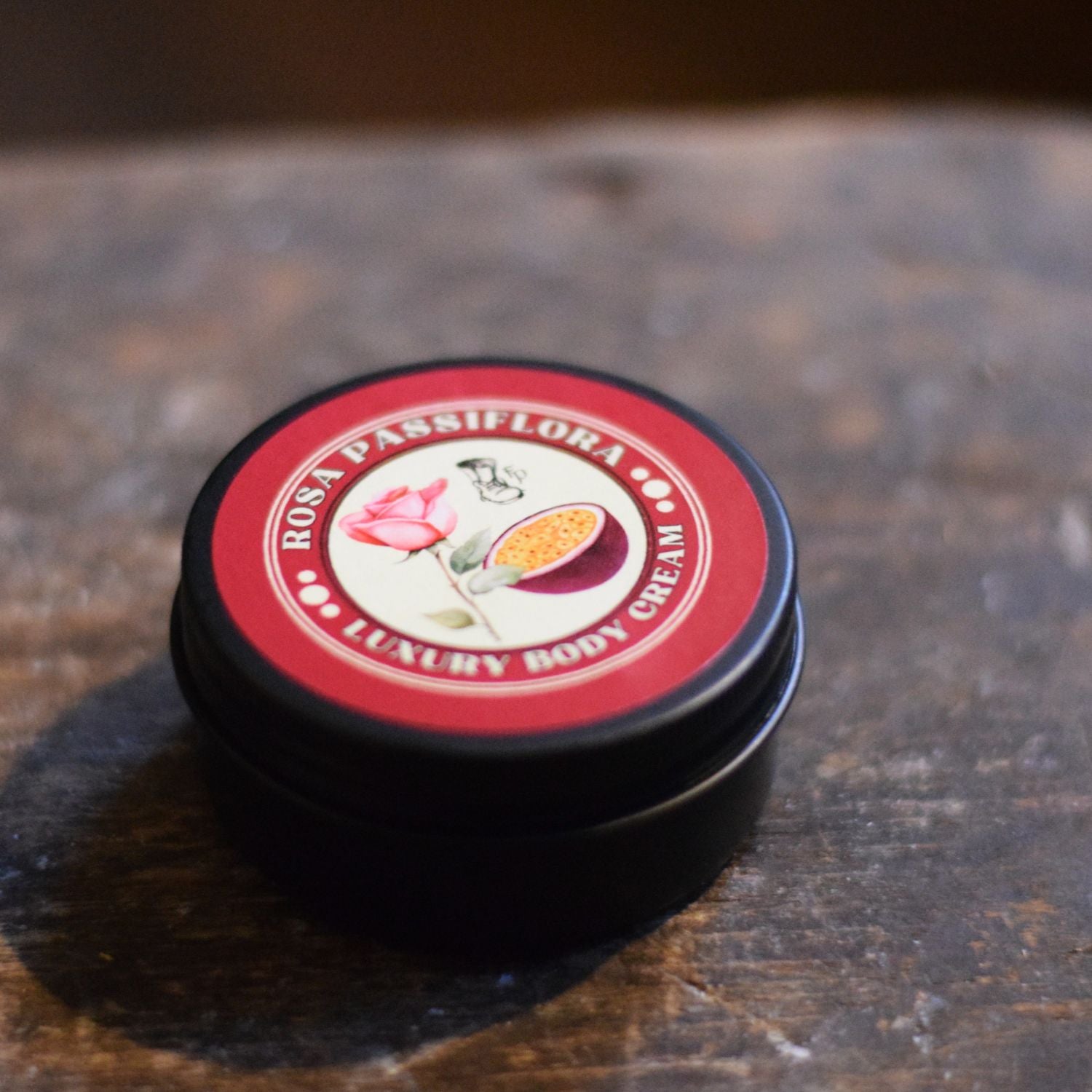 Two black tins with red lids featuring a floral design on a wooden surface