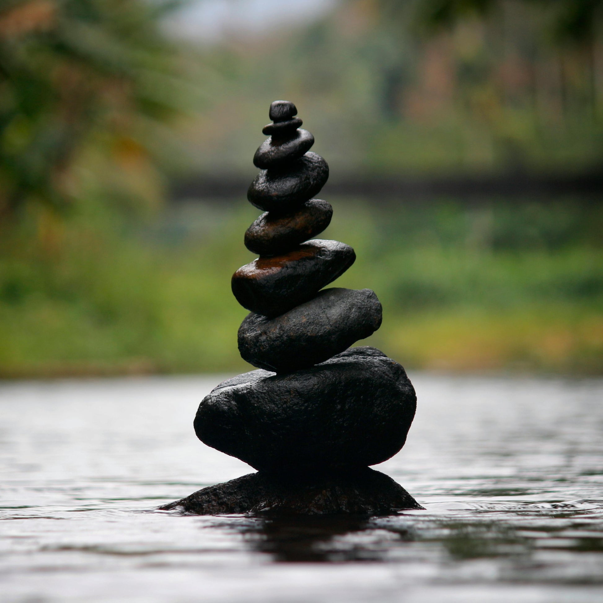Stack of black stones balanced on water with a blurred natural background