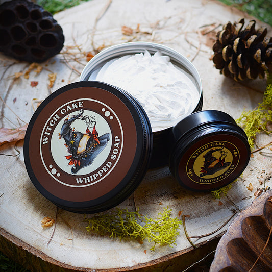 Witch Cake whipped soap in a container on a natural wooden surface with decorative elements.
